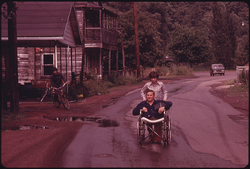 55. Jack Smith, 42, a Disabled Miner in Rhodell, West Virginia, Is Wheeled Down the Street by His Daughter, Donna, 16, to the Beer Joint He Operates 06/1974. Photographer: Jack Corn
