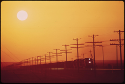 60. Transmission lines and railroad near Salton Sea. District of Los Angeles smog obscures the sun, May 1972. Photographer: Charles O'Rear